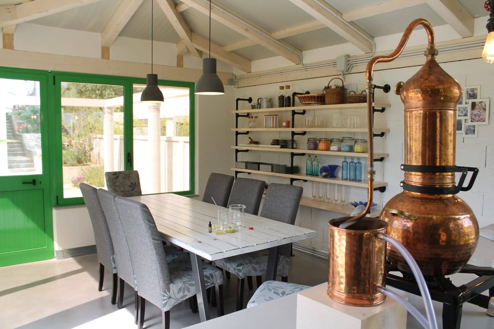 The workshop room with a hammered copper still, long table and shelves of jars